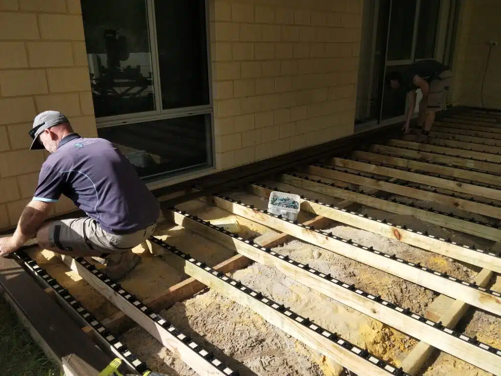 Landscapers installing timber decking subframe with hidden fastener clips alongside a residential home
