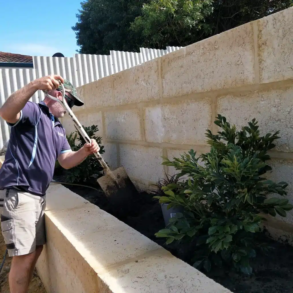 Landscaper planting shrubs in a limestone retaining wall garden bed during a residential landscaping installation